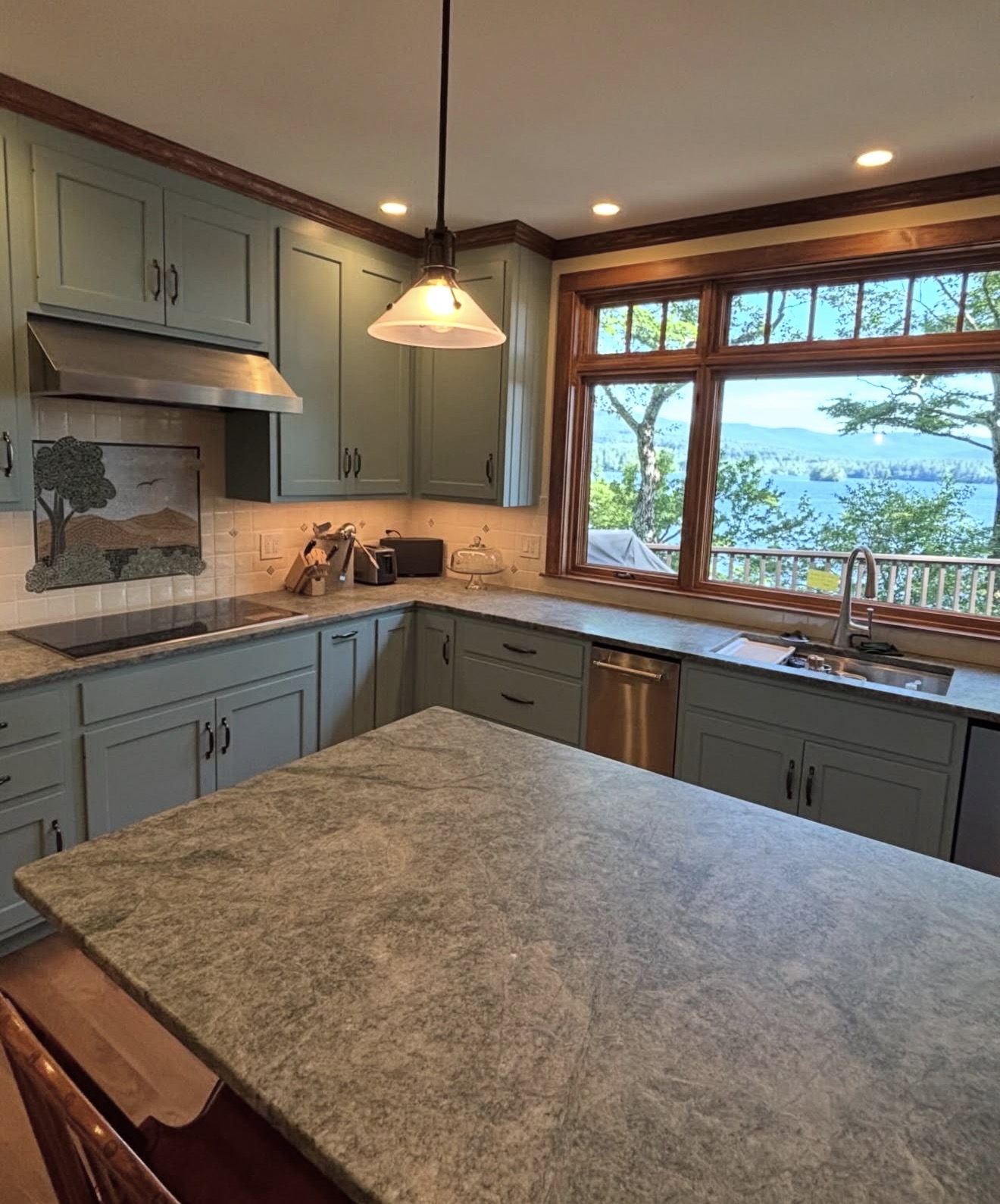 Sage-green custom kitchen with stone countertops, tile mural backsplash, and lake views in the NH Lakes Region