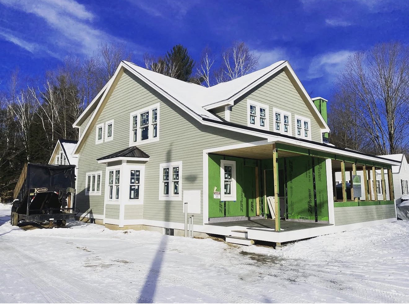 New custom farmhouse under construction in winter with gray lap siding and covered porch, New Hampshire
